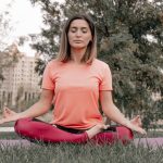Adult woman practicing meditation on a yoga mat outdoors in a tranquil park setting.