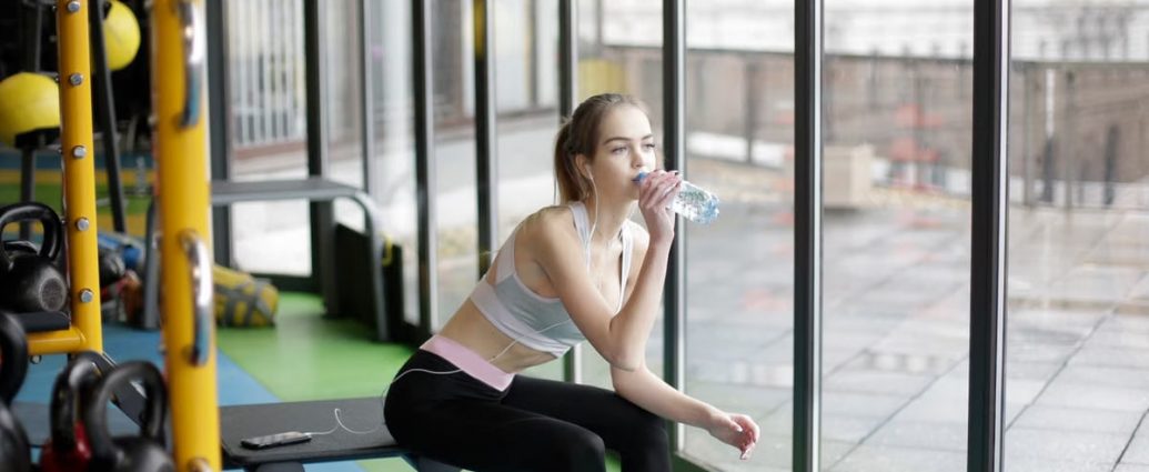 A young woman in activewear hydrates during her workout in a modern gym.