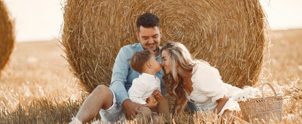 A happy family enjoying time together in a sunny, rural hay field, showcasing warmth and bonding.