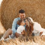 A happy family enjoying time together in a sunny, rural hay field, showcasing warmth and bonding.